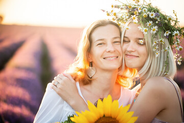 Mom and daughter are standing together in a purple lavender field. The friendly relationship of a teenage girl and a mother of a woman in transition. Two women communicate and smile at each other.