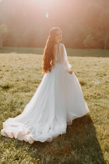 Fototapeta na wymiar Beautiful back of the bride in a wedding dress on the field at the sunset