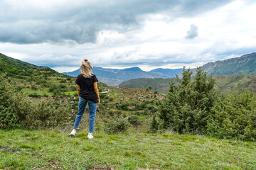 Naklejka premium A girl on the background of the village of Kurib in the Caucasus mountains, on top of a cliff. Dagestan Russia June 2021