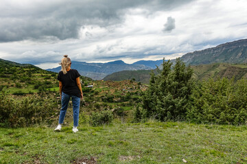 Naklejka premium A girl on the background of the village of Kurib in the Caucasus mountains, on top of a cliff. Dagestan Russia June 2021