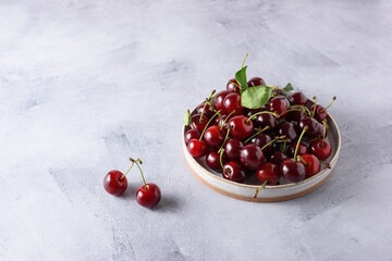 Berries of fresh cherries in a light ceramic plate on a gray concrete background. Place for text.