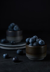 Fresh blueberries in a gray ceramic bowl on black concrete and black background.