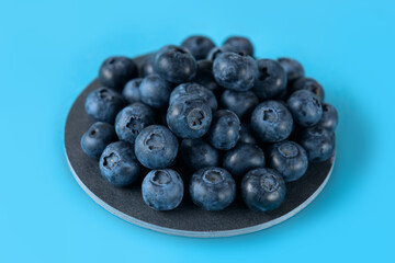 Fresh blueberries on a gray round ceramic board on a blue background. Horizontal.