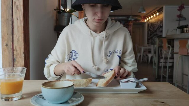a girl in a hoodie and a black hat spreads butter on white bread toast