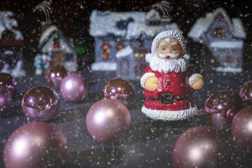 Small toy Santa Claus in snow drift in dark night with a village in the background.