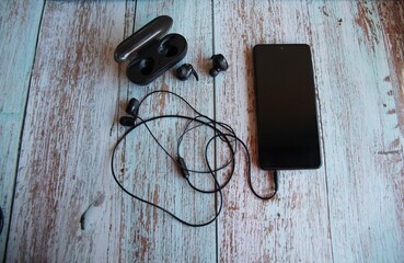 Wireless headphones, wired headphones and cellphone on a wooden table.