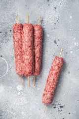 Raw kofta or lula kebabs skewers on butcher board. Gray background. Top view