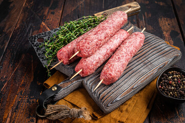 Fresh Raw kofta or lula kebabs skewers on wooden board with thyme. Wooden background. Top view