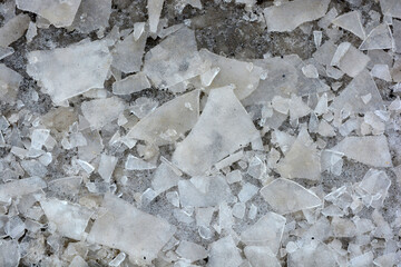 Broken transparent ice, small pieces of ice crust lie near a frozen puddle and float in the water. Spring is warming, the ice is melting on the street. 