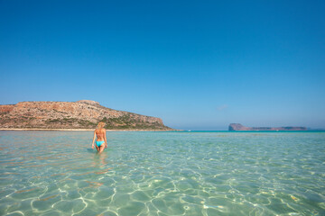 Fototapeta na wymiar Cheerful woman enjoying walking in shallow water in sea. She is in turquoise water