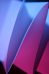 Pliegues en forma de triàngulos de la hoja de papel con luz incidente de color azul y rosa, forman un bello diseño abstracto de luces y sombras en fondo negro