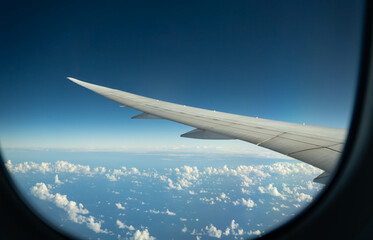 Wing of an airplane flying over morning clouds. View on cloud and blue sky through the airplane window.