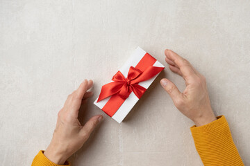 Gift box with a red ribbon in female hands. Happy birthday or holiday concept.