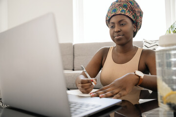Black African woman studying online at home, traditional headscarf