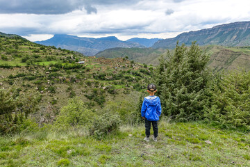Naklejka premium A boy on the background of the village of Kurib in the Caucasus mountains, on top of a cliff. Dagestan Russia June 2021
