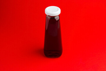 Bottle with red liquid halthy beverage on red pepper background. Cherry juice
