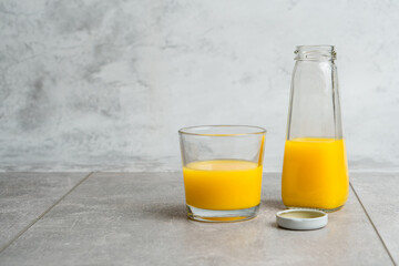 Bottle and glass with yellow liquid juice halthy beverage on gray concrete background. Orange fresh