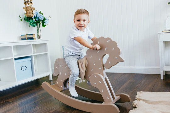 A little boy rides a rocking horse in a children's room. Light interior