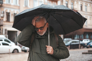 Headache in a mature man outdoors. Senior man under umbrella during doja with migraine.