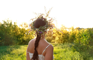 girl in flower wreaths on meadow, sunny green natural background. Floral crown, symbol of summer...