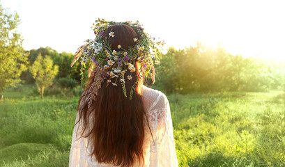 girl in flower wreaths on meadow, sunny green natural background. Floral crown, symbol of summer...