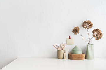 Empty desk, white table with minimal vase with a decorative dried branches against white wall.