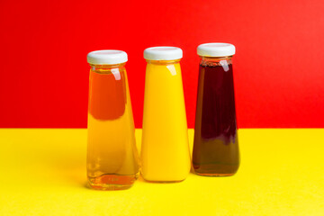 Bottles with yellow and red liquid halthy beverage on yellow and red background. Orange apple cherry