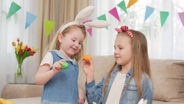 little girls with rabbit ears play with Easter eggs in game of who will break.