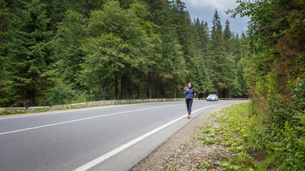 Young fitness woman running on the road through the forest