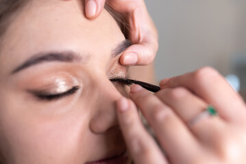 Make-up artist applies eyeliner to the girl's upper eyelid with a brush - obrazy, fototapety, plakaty