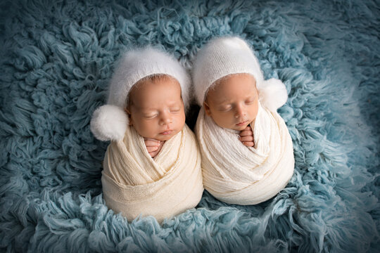 Tiny newborn twin boys in white cocoons on a blue background in white caps. Studio professional photography of newborn twins.