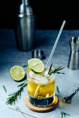 Alcohol cocktail with lime slice rosemary ice and shaker jigger on black background. Party time