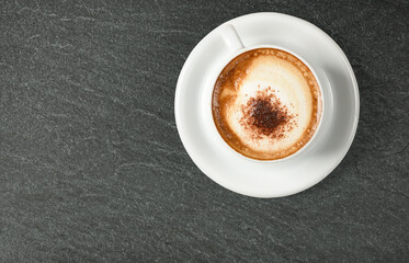 Cappuccino coffee garnished with chocolate powder in white ceramic cup on granite stone surface
