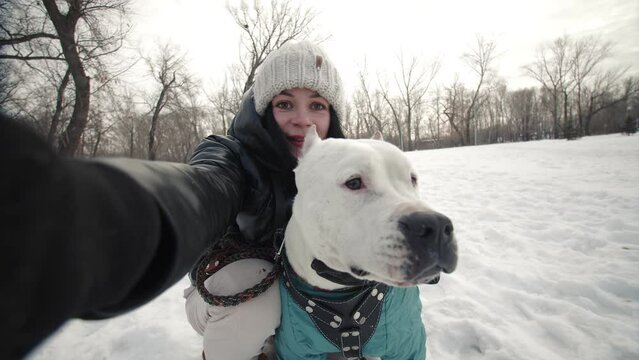 Woman takes pictures in winter of herself and pitbull dog on smartphone camera taking selfie, front view. Woman is photographed with dog on smartphone. Concept of owner and pet