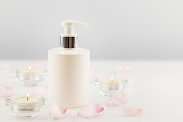Fototapeta na wymiar White cosmetic bottle, rose petals and candles on a white table