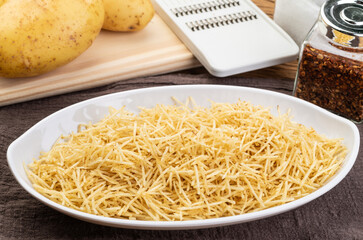 Potato straw or shoestring potato in a white plate with raw potatoes