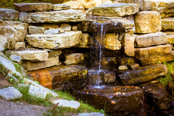 Small artificial waterfall made of granite stones. A waterfalls made of artificial rock in the state park. Cold mountain water flowing down the rocks in the river on nature outdoors. Landscape design.