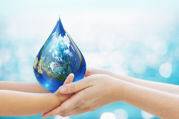World water day concept . baby Hand and Mom hand Holding Earth in Water Drop shape on Blue Bokeh background.Copy Space on horizontal sheet.Clipping path.Elements of this image furnished by NASA