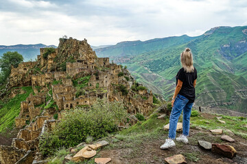 Naklejka premium A girl on the background of Gamsutl village in the Caucasus mountains, on top of a cliff. Dagestan Russia June 2021