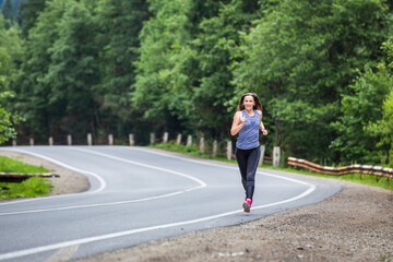 Runner woman running on the mountain road through the forest.