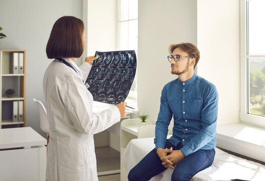 Female doctor in modern clinic gives young man his X ray image. Radiologist with Xray radiograph talking to male patient. Man listening to medical specialist's explanation, advice and recommendations