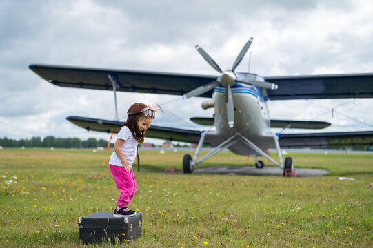 A cute little girl playing on the field by a four-seater private jet dreaming of becoming a pilot