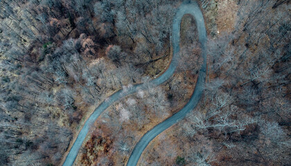 Aerial high angle view of narrow winding curvy mountain road among the trees in winter forest. Bird's eye view landscape.