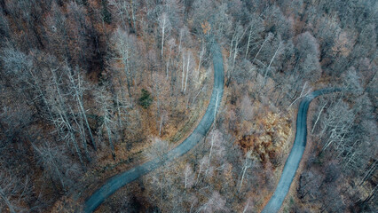 Aerial high angle view of narrow winding curvy mountain road among the trees in winter forest. Bird's eye view landscape.