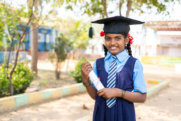 Happy girl kid in uniform standing by dreaming about graduation while holding graduation...