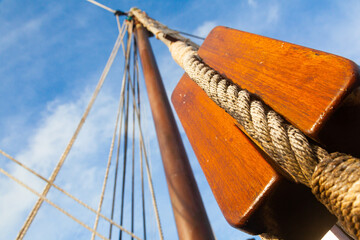 Ancient wooden pulleys of a sailing ship with knotted ropes against the sky.