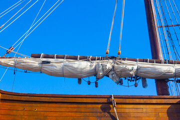 An old wooden caravel ship with folded sails against a blue sky with white clouds.