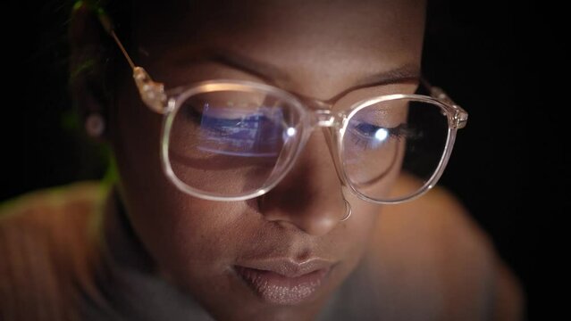Close-up of the reflection of the computer screen on the glasses of a woman working with a laptop in the dark. Concept of computer network security and the Internet.