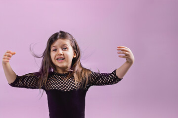 Portrait of a child of a girl of five years of a shocked crazy smiling girl raising her arms and hair. Close-up of a baby girl on a pink background