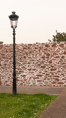 Farola junto a muro de piedra rocosa rojiza en centro de pueblo europeo